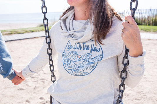 Model wearing an oatmeal-colored funnel neck hoodie with side pockets and relaxed fit, styled casually for a cozy coastal look by Coral Anchor Apparel.
