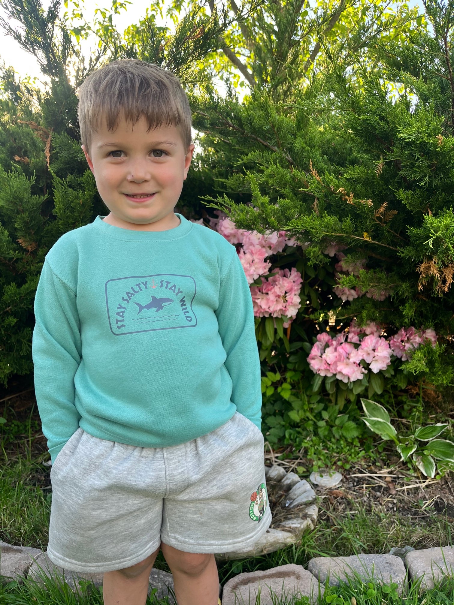 Toddler wearing a saltwater blue crewneck sweatshirt with a playful shark graphic and the words "Stay Salty, Stay Wild" printed on the front