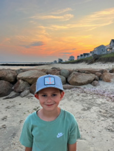 child wearing the Weekender Snapback Hat with Coral Anchor PVC patch, standing on the beach with ocean in background.
