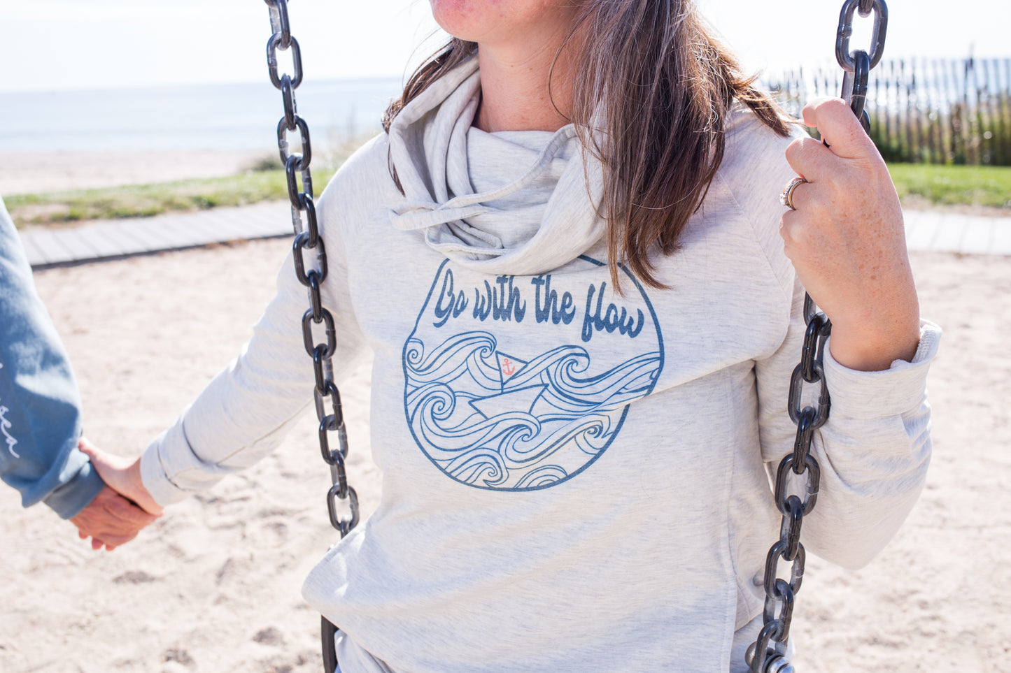 Model wearing an oatmeal-colored funnel neck hoodie with side pockets and relaxed fit, styled casually for a cozy coastal look by Coral Anchor Apparel.
